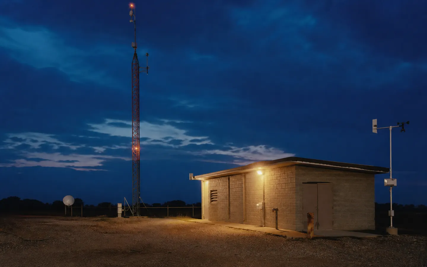 A rural radio relay tower and equipment building at dusk